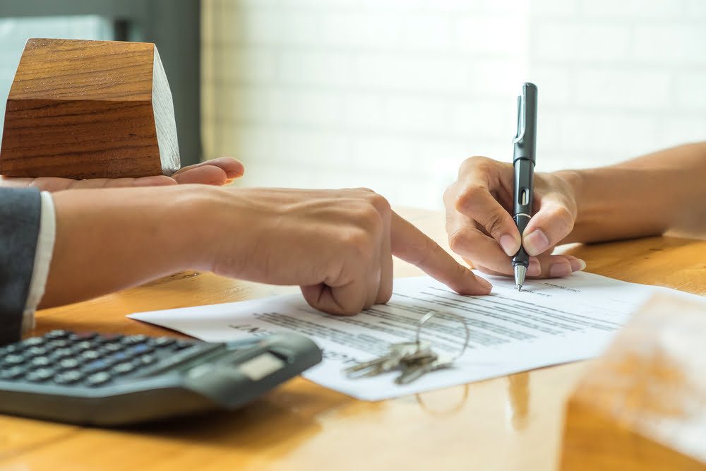 buyers are signing a home purchase agreement from a broker,model house in broker hand and calculator with a house key on the table