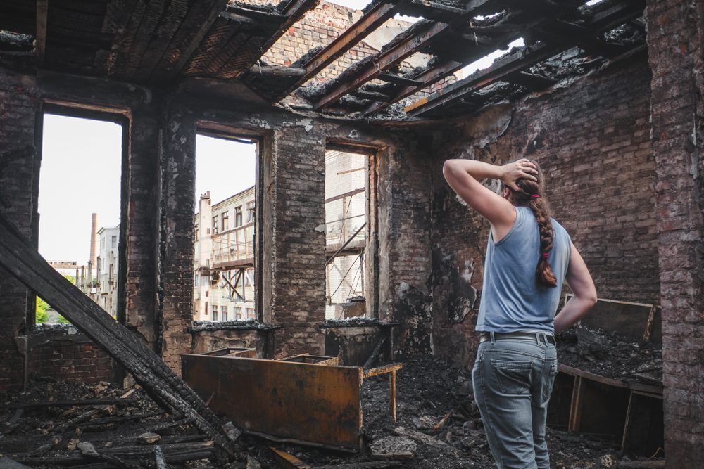 sad man holds his head by hand and cry in burnt out house after disaster