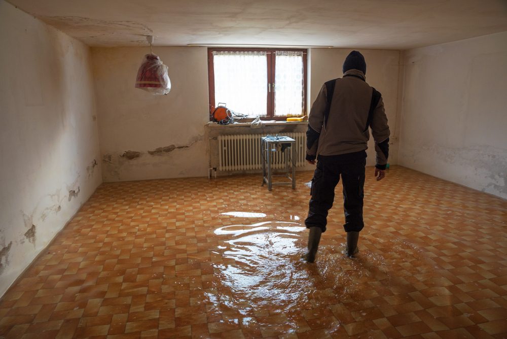 Man walks with rubber boots in a flooded tiled basement during flood