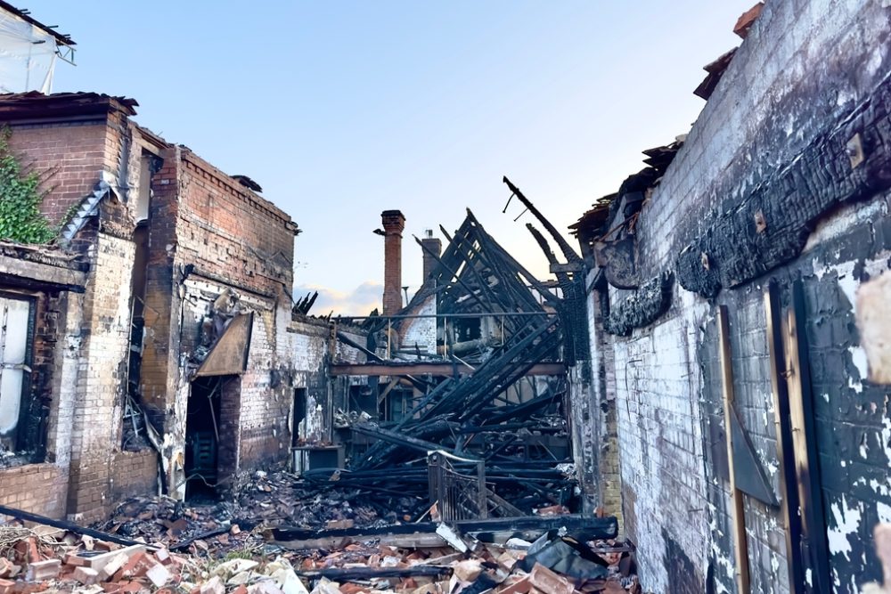 The charred burnt out remains of a fire damaged building with rubble on the ground
